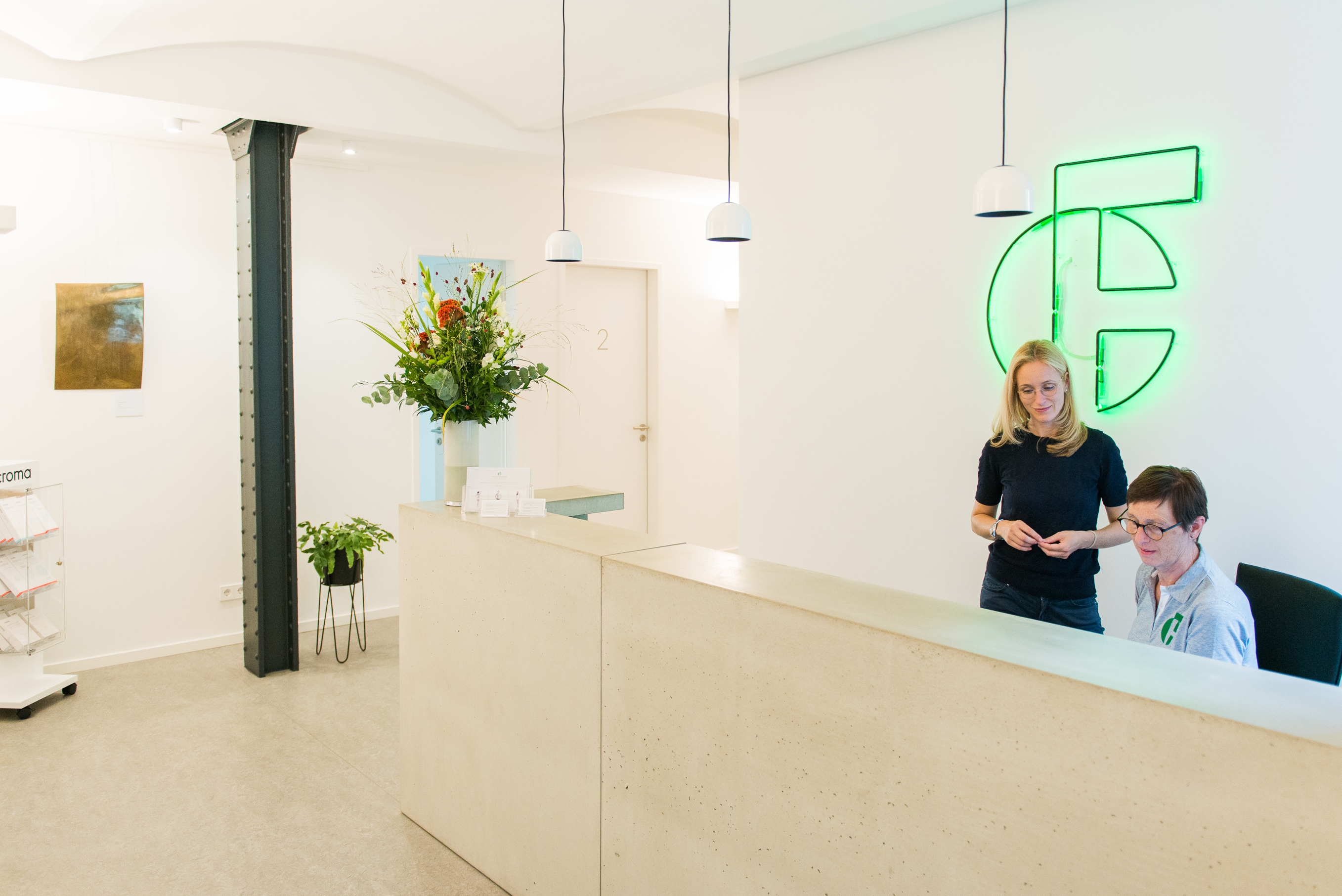 The reception desk of the Finke & Frantzen practice with the green neon logo and the practice team